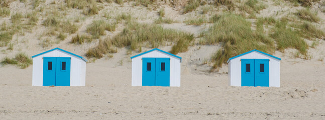 Four colorful beach huts stand in a row on the sandy shore of Texel, Netherlands, under the bright...