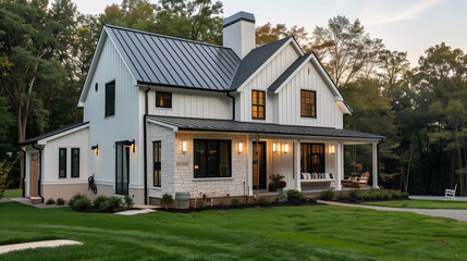 Naklejka premium A new, white modern farmhouse with a dark shingled roof and black windows. The left side of the house is covered in a rock siding