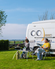 Two individuals are seated in front of their RV, enjoying the peaceful surroundings of a grassy...