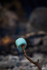 Close-up shot of a marshmallow skewered onto a stick, being held over a flaming charcoal fire