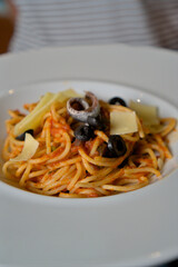 Person holding a plate of spaghetti with olives, cheese shavings, and anchovies, perfect for culinary blogs and restaurant promotions with copy space.