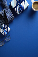 Flat lay composition featuring a gift, neckties, eyeglasses, and a cup of coffee on a vibrant blue...