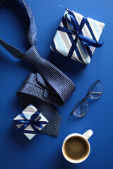 Flat lay composition featuring a cup of coffee, two gift boxes, glasses, and a neatly folded blue...