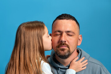 Parenthood. Portrait of child, little girl kissing her beloved father to cheek against blue studio...