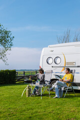 Two individuals sit outside a camper van, surrounded by lush green grass in Texel, Netherlands....