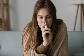 rhinitis, medicine and healthcare concept - close-up of sick woman using nasal spray on sofa at...
