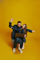 Business Partners. dad and his daughter collaborate over laptop, with joyful expression raising hands against sunny-yellow background. Concept of Father's day. Children's day, Family day, parenthood.
