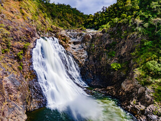 a waterfall flowing over a lush green hillside next to a forest: Wujal Wujal Falls