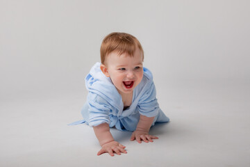 A cute happy laughing baby in a soft bathrobe crawls on a white background after bathing. The child is wrapped in a clean and dry towel. Washing, baby hygiene, health and skin care