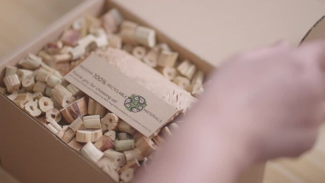 A woman places a "100% Recyclable Materials" label on a cardboard box filled with eco-friendly water hyacinth cushioning, demonstrating sustainable and environmentally friendly business practices
