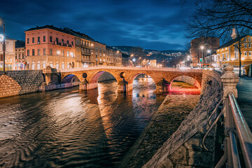 Sarajevo's old town at dusk, where the iconic Latin Bridge and traditional houses along the Miljacka River create a picturesque view of the city's historical charm.