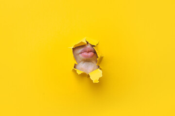 A child's lips appear in a torn hole of yellow paper. Imitation of a kiss. Silence concept.