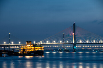 Majestic vessel illuminated under a grand bridge in a tranquil evening setting in Wuhan, China.