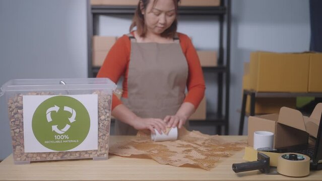 The focus is on a label stating "100% Recyclable Materials" highlighting the sustainable practices of a small business, In the background, a woman wraps a product with eco-friendly honeycomb paper