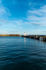 Obraz premium Group of boats around a lighthouse on a sunny day with a cloudy blue sky in the background