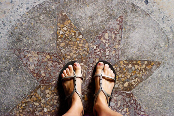 Female feet in summer sandals on a beautiful decorative granite floor with a star pattern close-up, top view. Travel through old abandoned buildings
