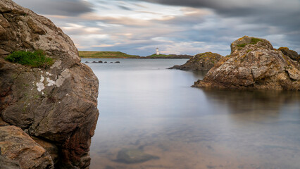 Scenic view of a lighthouse amidst rocks by the shore on a cloudy day