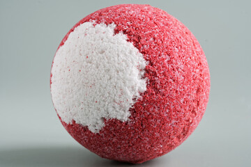 Large, two-tone, red and white bath bomb on a light pastel background. Porous surface of the sphere. Imitation of a mysterious planet. Photo. Selective focus.