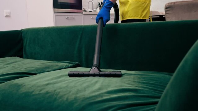 in an apartment cleaner in a yellow apron does a steam cleaning of a green sofa with professional equipment