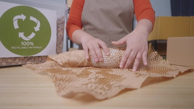 Close up of A woman wraps a product with eco-friendly honeycomb paper with label stating "100% Recyclable Materials" highlighting the sustainable practices of a small business, Slow Motion