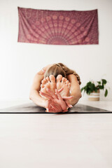 A woman practices yoga, she is bent on the floor holding her feet with her hands in gyan mudra
