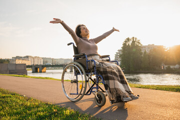 Happy senior woman in wheelchair raised hands enjoying freedom walking on road in city park...