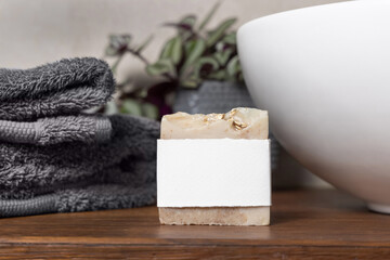 Soap bar with blank label near grey towels, plant and basin on wood in bathroom, mockup