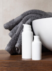 White pump cosmetic bottles near grey folded towels and basin on wooden countertop in bath, mockup