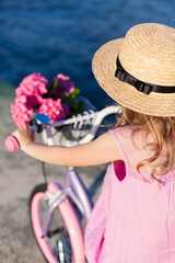 Child girl riding bike on sea beach. Kid in straw hat and dress cycling on sunny coastline. Pink...
