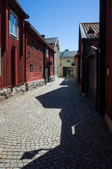 Empty alley in the old town of Västerås, traditional Swedish red wooden houses, the shadow of the buildings creates a quirkiest shadow on the cobbled street, Architecture of Scandinavia