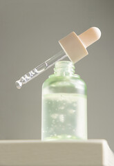 Drop falls from a pipette resting on a bottle filled with green serum agains gray, macro