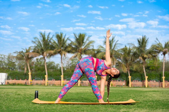 Young indian woman doing Triangle , Utthita Trikonasana yoga pose in her garden. exercise, healthy lifestyle, sports, workout, meditation, mental health concept.