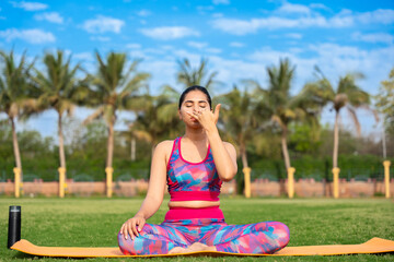 young indian woman doing Anulom Vilom Pranayama yoga pose in garden. sports, workout, meditation, well being, mental health, international yoga day concept.