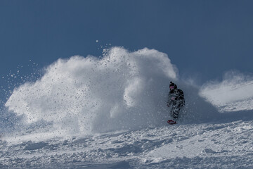 A snowboarder rides out of a cloud of snow breaking in pieces after performing a powder turn on an untouched slope
