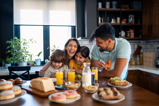 Two happy kids, boy and girl enjoying eating breakfast with parents. Smiling beautiful mother laughing and having fun with her kids and husband during breakfast at home.