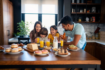 Cheerful couple bonding and embracing with children during breakfast time at kitchen table at home.