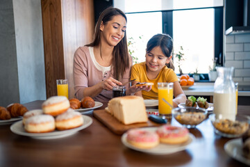 Smiling woman making breakfast to her adorable small daughter. Lovely small girl having marmalade...