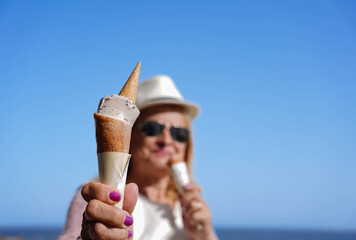 mature woman wearing sunglasses tasting two ice cream . Diabetes and obesity concept in summer