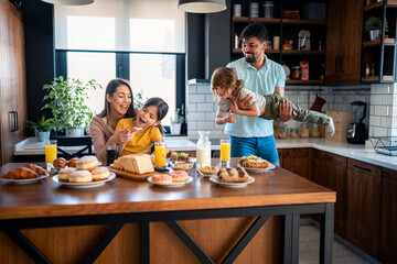 Young parents with small children having fun during breakfast. Mother and father at breakfast with...