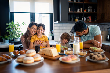 Small boy and girl with parents at kitchen table enjoying breakfast at home in the morning. Family...