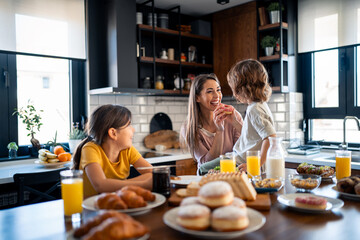Cute little boy and girl eating breakfast, sitting at table with happy mother at home.