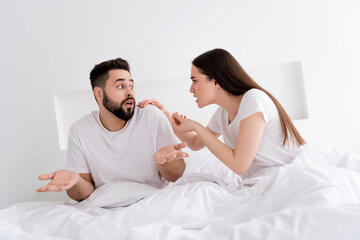 Photo of unhappy uncertain couple wear white t-shirts having conflict indoors apartment bedroom