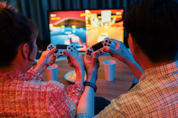Couple gamer with controlled joystick playing car racing video game together on tv screen with...