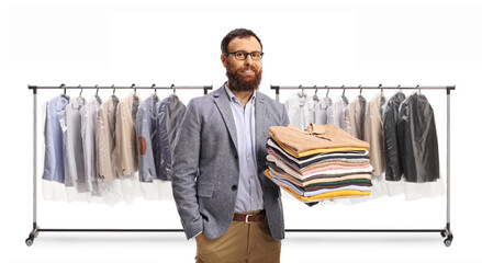 Man holding a pile of folded clothes in front of a rack with clothes on hangers