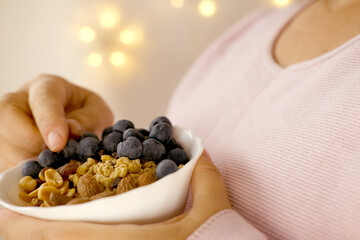 close-up female hand takes berries on blurred background with bokeh, healthy food white cup,...