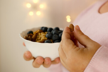 close-up female hand takes almonds on blurred background with bokeh, healthy food white cup,...