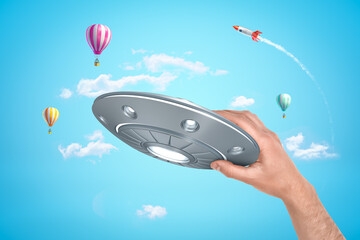 Hand holding UFO with airlifted balloons and rocket