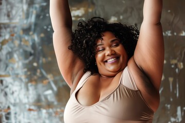 A joyful woman with curly hair and a radiant smile, stretching her arms upward. She is wearing a beige top against a blurred background.