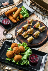 Assorted snacks, deep fried cheese balls breaded, cheese nuggets, canapes sausages in cheese on rustic background. Appetizer, top view