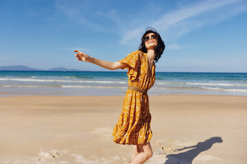 Woman in yellow dress with arms outstretched standing on beach with serene expression on face...